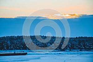 Winter sunset over the field with trees in the foreground.