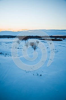 Winter sunset over the field with trees in the foreground.