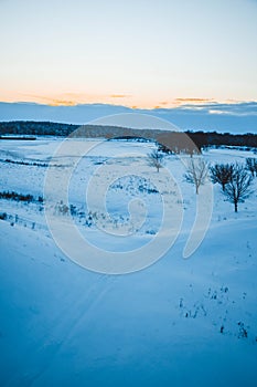 Winter sunset over the field with trees in the foreground.