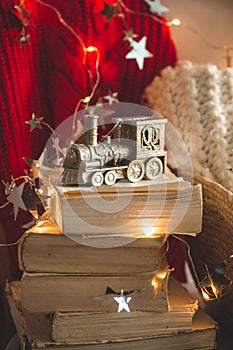 Winter sweater laid on a chair with a books and locomotive, train of Christmas decorations. Coniferous branch and garland, closeup