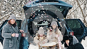 winter tea picnic. Happy family is having tasty snack, a tea party with cream, outdoors. They are sitting on car trunk