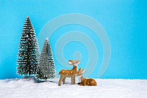 Winter theme with miniature reindeers and Christmas trees on blue background with copy-space