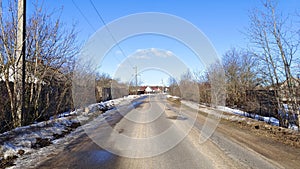 In winter, there is snow on the ground. Under the rays of the bright sun, the snow melts on the asphalt road. Along the road are h