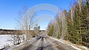 In winter, there is snow on the ground. Under the rays of the bright sun, the snow melts on the asphalt road. Along the road are t