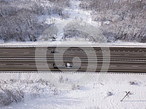 Winter time aerial top down view of a snowy road surrounded pine tree forest