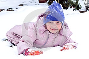 Winter is a time of play and pleasure: an eight-year-old smiling girl in a pastel jacket and a blue hat makes snowballs in a