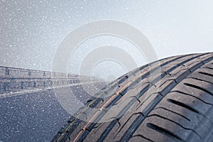 Winter tire in the foreground is on a road that is snowing