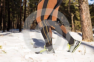 Winter trail running: man takes a run on a snowy mountain path in a pine woods.