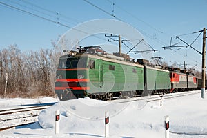 Winter train leaves the forest and approaches the station crossing, railway power line