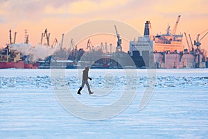 Winter. Urban landscape. A man walks on ice in background of the seaport