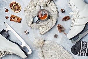Winter vacation concept. Skates warm clothes, Cup of hot tea with fragrant spices on grey background.