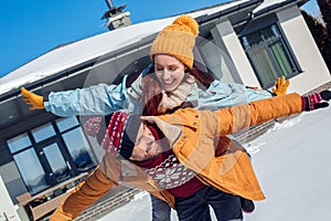 Winter vacation. Young couple standing together outdoors near house making flying pose laughing playful