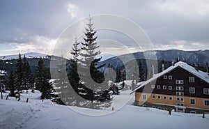 Winter view overlooking a lodge in the mountains surrounded by evergreens and snow on a cloudy day, in Ranca resort, Romania