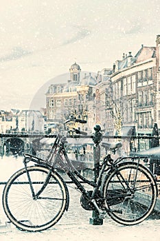 Winter view with snowfall of the Dutch Nieuwe Rijn canal with bridge and bicycle in the city center of Leiden