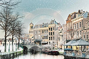 Winter view with snowfall of the Dutch Nieuwe Rijn canal with bridge and historic buildings in the city center of Leiden photo
