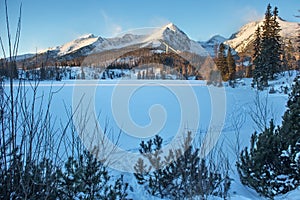 Winter view of the snowy Stbske Pleso lake surrounded by the mountains.