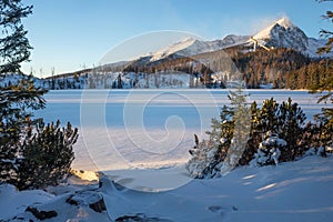 Winter view of the snowy Stbske Pleso lake surrounded by the mountains.