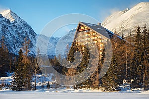 Winter view of the Strbske pleso village with hotel, coniferous forest and snowy peaks.