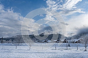 Winter village landscape, wooden houses and church in the countryside in fog at sunset in mountains