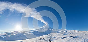 Winter volcanic landscape, panoramic view of eruption active volcano plume gas, ash from crater in sunny day with blue