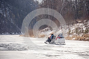 Winter walk with family on a snowmobile on a frozen river. A snowmobile with a trailer rolls children on the ice of the