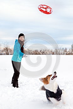 Winter walk in the snow, woman is playing flying disc or frisbee with her dog