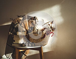 Winter warm blanket on a chair with a basket of Christmas decorations, books and led string lights. HOME. Winter reading. House