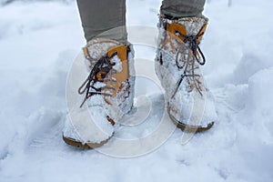 Winter warm boots in the snow. Shoes are covered with snow. Low Section Of Man Standing On Snow Covered Field. Walking