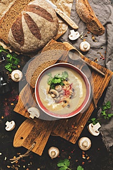 Winter warming soup. Mushroom cream soup with homemade rustic bread on a dark background. View from above,overhead