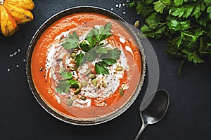 Winter warming spicy pumpkin soup with seeds, cream, pepper and parsley. Healthy comfort slow food. Soup bowl on black table