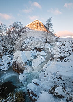 Winter waterfall at the foot of a snow-capped mountain with a morning sunlit peak