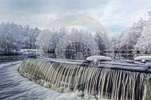 Winter waterscape. Waterfall, snow-covered trees