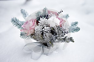 Winter wedding bouquet of pink roses, pine cones and christmas tree branches on snow, copy space.