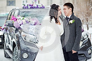 Winter wedding, the happy couple before the decorated car on a snowy street. Bride and groom look at each other.