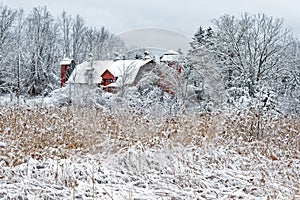 Winter white snow on red barn with silo and field or meadow