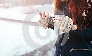 Winter. Woman with red hair wearing gloves . Girl drinking hot tea or coffee with iron insulated cup. It uses a phone or