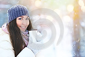 Winter young woman portrait. Beauty Joyful Model Girl holding thermocup with hot tea and smiling, having fun in winter