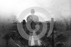 A winters day and a semi transparent male figure standing above a stream in the countryside. With a blurred, textured, weathered,