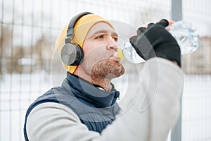 Wintertime Hydration A determined runner, headphones on, He is seen taking a quick break to hydrate