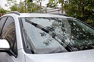 Wipers cleaning raindrops from car windshield outdoors