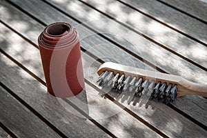 Wire brush and sandpaper lying on wooden garden table before sanding