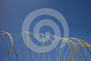 Wire circle mesh metal fence, sharp with razors, barbed. Clear blue sky background, close up view.