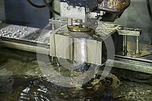 The Wire EDM machine cutting the die parts with liquid coolant.