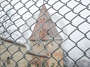 Wire fence covered with hoarfrost or rime ice on a misty morning with a old medieval tower in the background