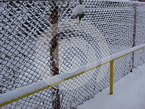 Wire fence in the snow.  Metallic net with snow. Metal net in winter covered with snow. Wire fence closeup. Steel wire mesh fence