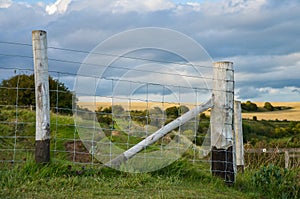 A wire fence with wooden pales around fields