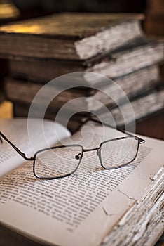 Wire framed reading glasses on resting on pages of open book with vintage, old books in background