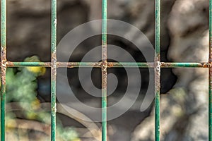 Wire mesh fence closeup photo. Green bush and huge cave in blurred background. Thin pillars. Decorative board front of garden.