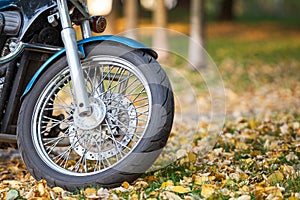 Wire-spoked wheel of a classic motorcycle standing on yellow leaves in autumn park, copy space photo