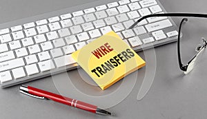 WIRE TRANSFERS text on a sticky with keyboard, pen glasses on grey background